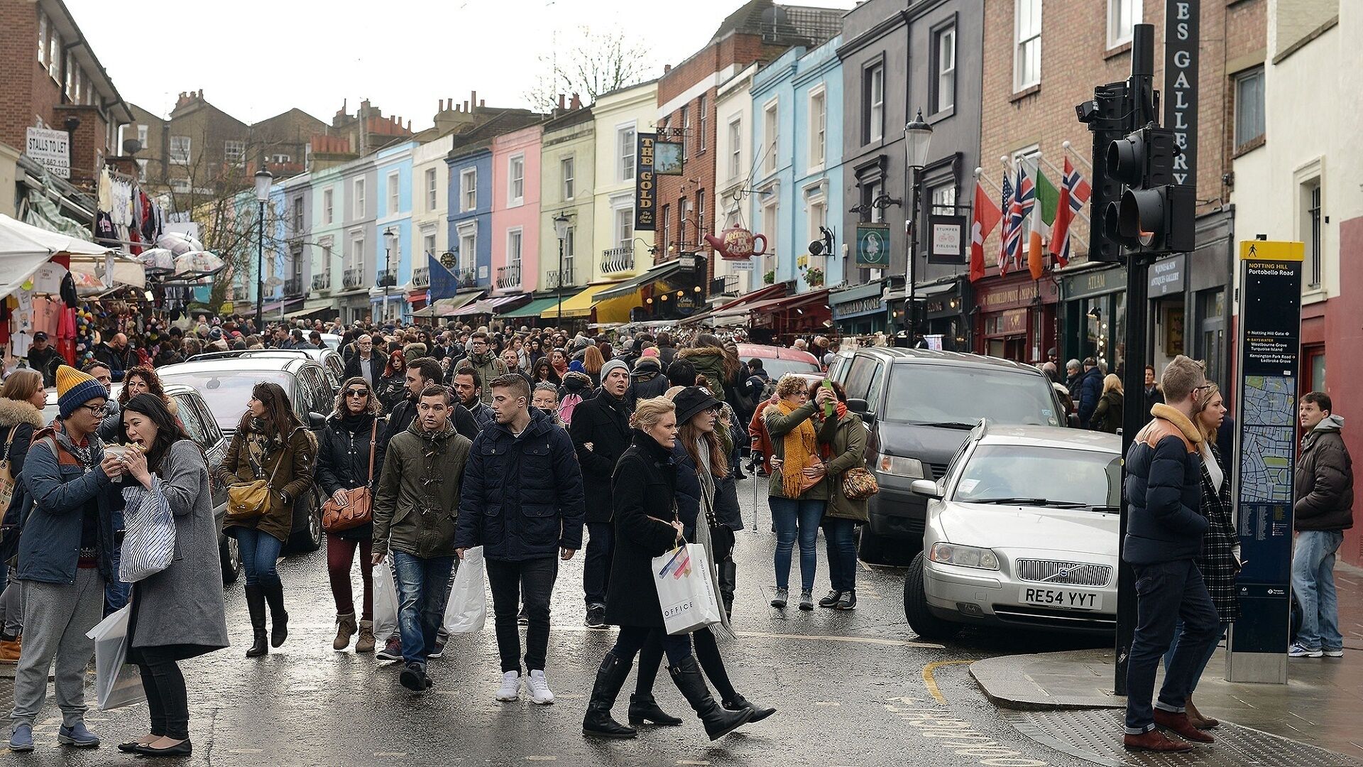 A crowded street scene with people walking and cars parked along the road.