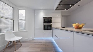 Una cocina moderna con armarios blancos, horno integrado y ventana con persianas.