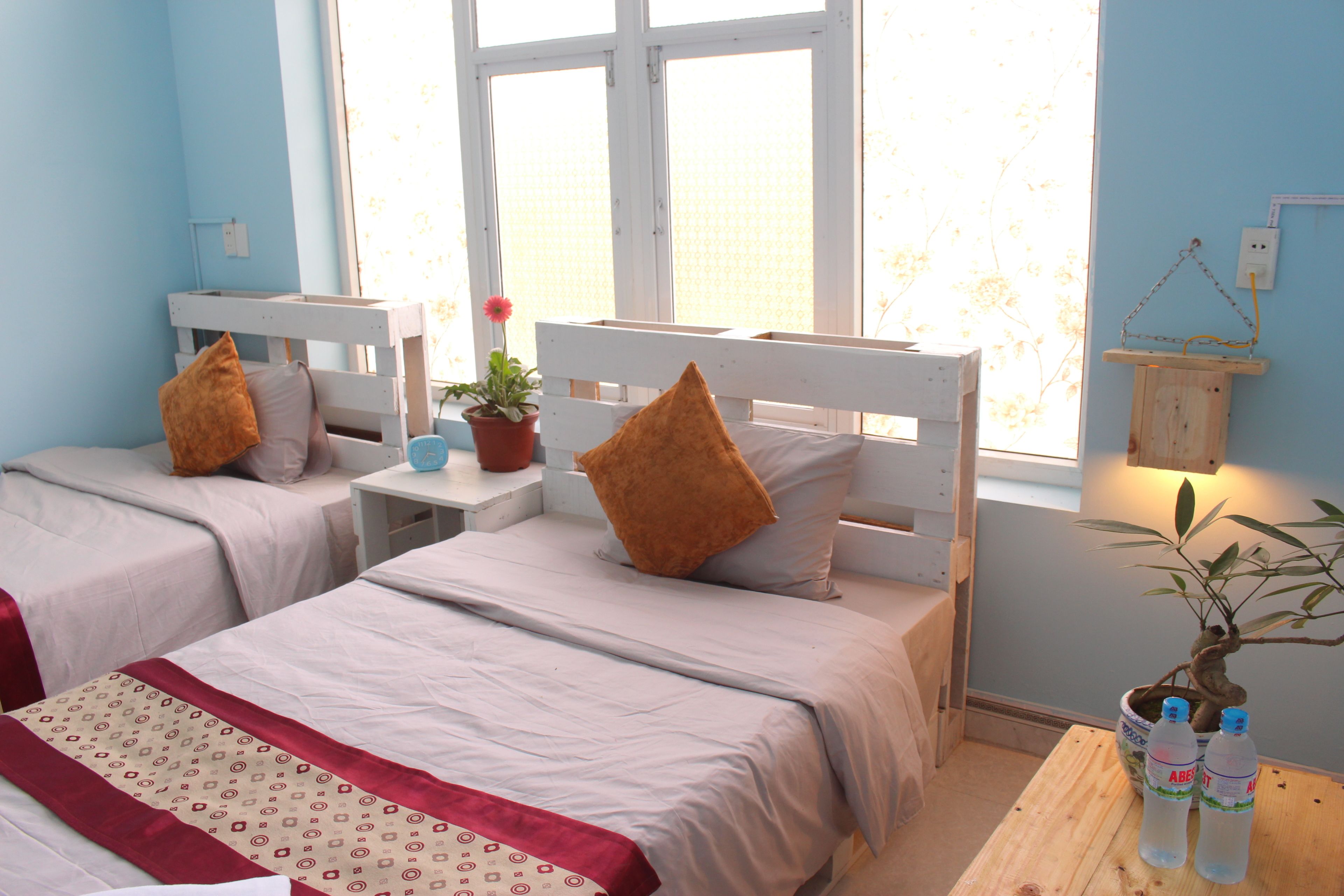 Une chambre avec deux lits, une petite table sur laquelle est posée une plante en pot, et une fenêtre donnant sur des arbres.