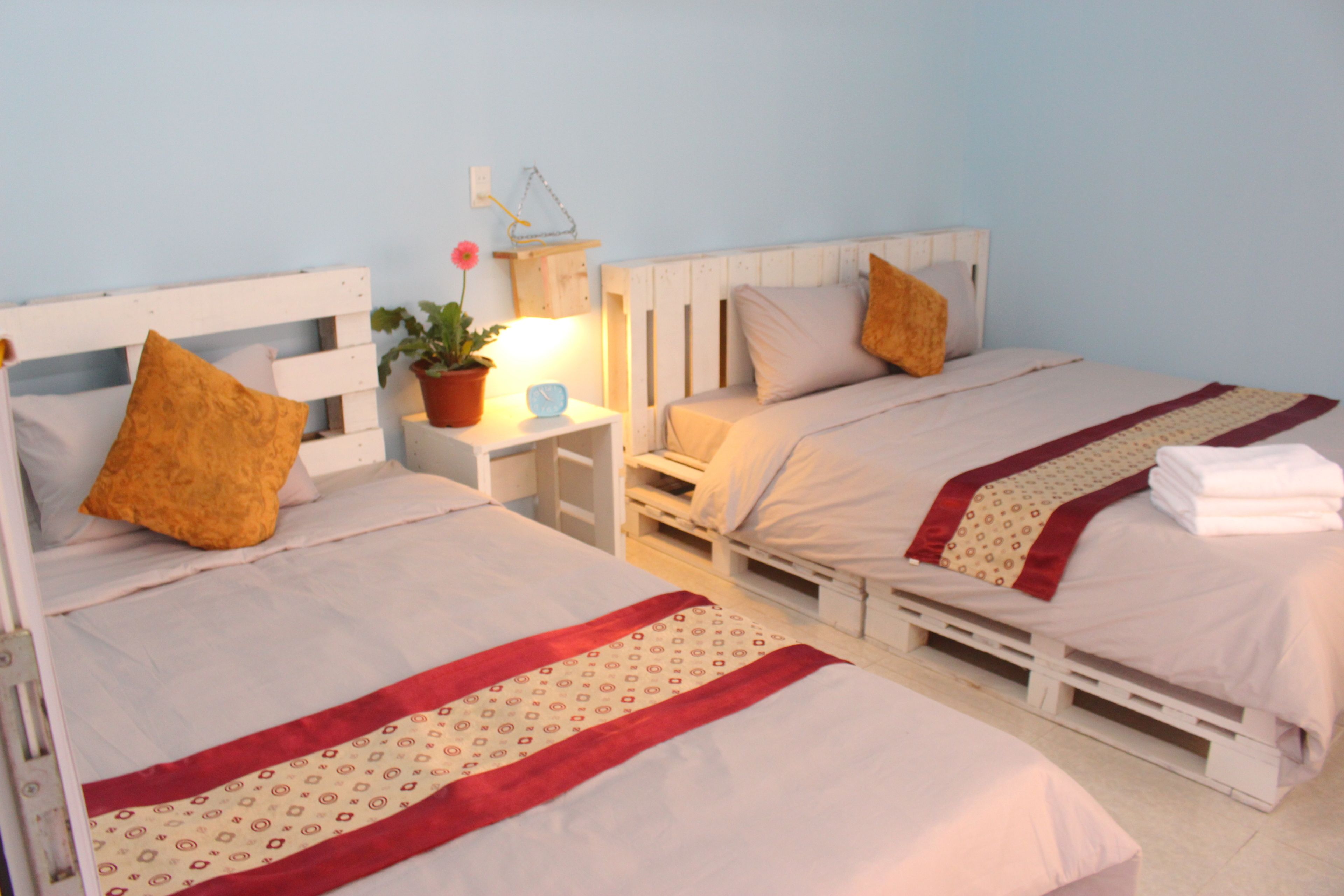 Dos camas individuales con estructura de madera, ropa blanca y mantas estampadas en rojo y beige.