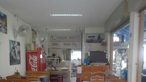 Un comedor con mesas y sillas de madera, un refrigerador de Coca-Cola y un letrero que dice 'Pizza Italy'.