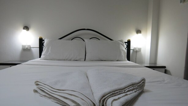 Una cama bien hecha con sábanas y almohadas blancas, dos lámparas de noche y un enchufe en la pared.