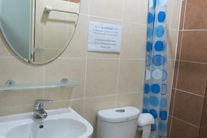 Et badeværelse med vask, toilet og spejl. Et skilt viser, at der ikke må skylles skrald eller bind ud i toilettet, men at der skal bruges skraldespanden.