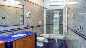 A bathroom with a blue-tiled floor, a wooden vanity, a white sink, a toilet, and a glass-enclosed shower.