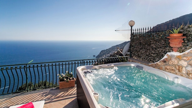 A hot tub with a view of the ocean, a stone wall, and a satellite dish.