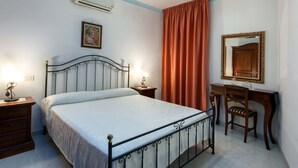 A bedroom with a bed, bedside tables, a desk with a chair, a mirror, and an air conditioning unit.