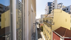 A narrow street between buildings with balconies, a visible fire escape, and a clear sky.
