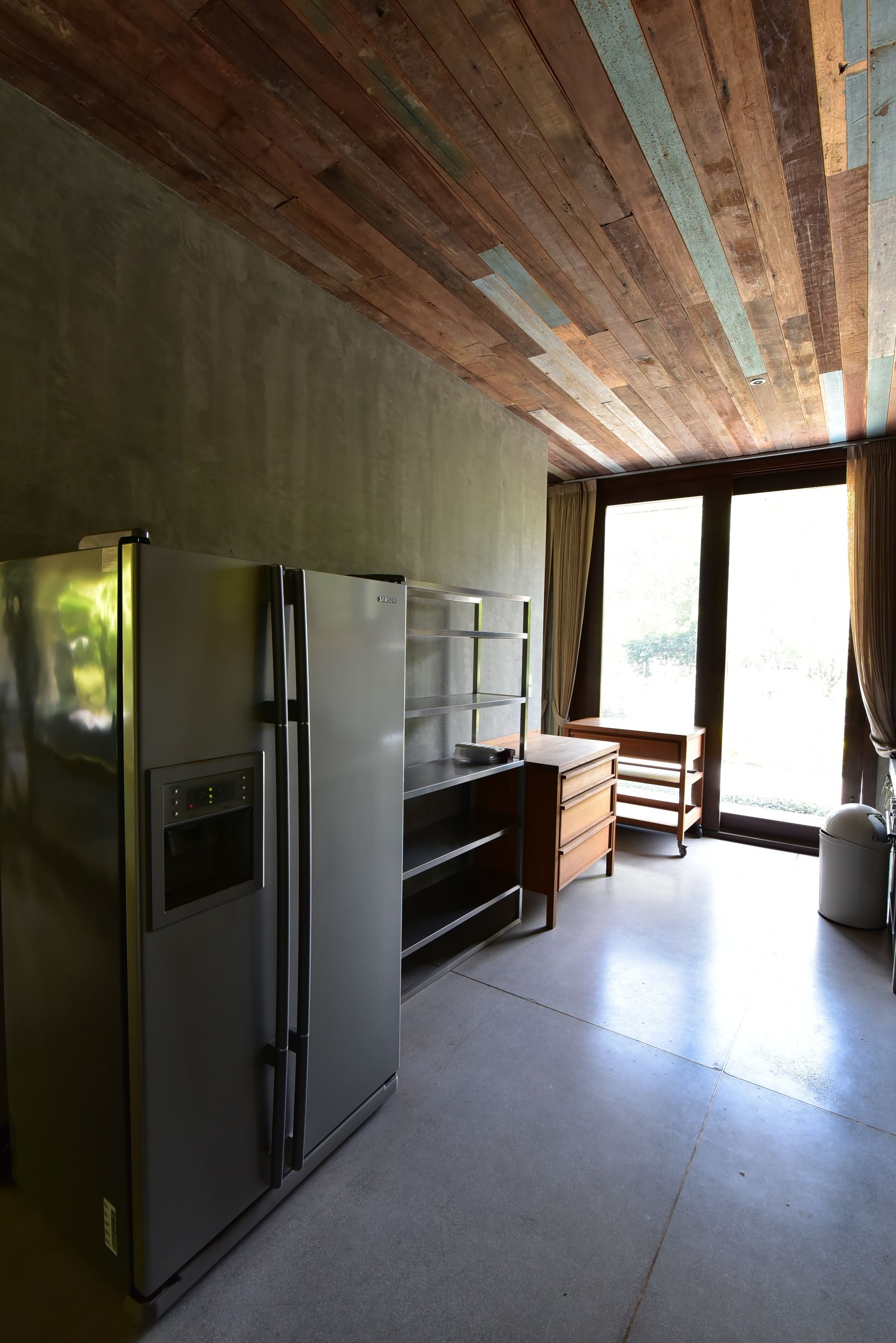 A compact kitchen with a stainless steel refrigerator, wooden cabinets, and a window providing natural light.