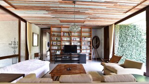 A spacious living room with a wooden ceiling, a large bookshelf, a television, and a comfortable seating area. - Uncle Jo Ranch (Pak Chong)