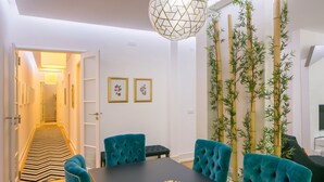 Un espace repas avec une table noire, des chaises de couleur turquoise, un tapis à motifs et un luminaire décoratif.