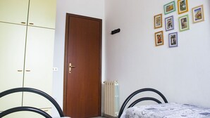 Een slaapkamer met een houten deur, een radiator, een bed met een beddengoed met een patroon, en een muur met ingelijste foto's.