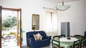 Een kamer met een blauwe bank, een eettafel met stoelen, een spiegel en een koelkast.