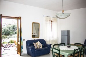 Une pièce avec un canapé bleu, une table à manger avec des chaises, un miroir et un réfrigérateur.