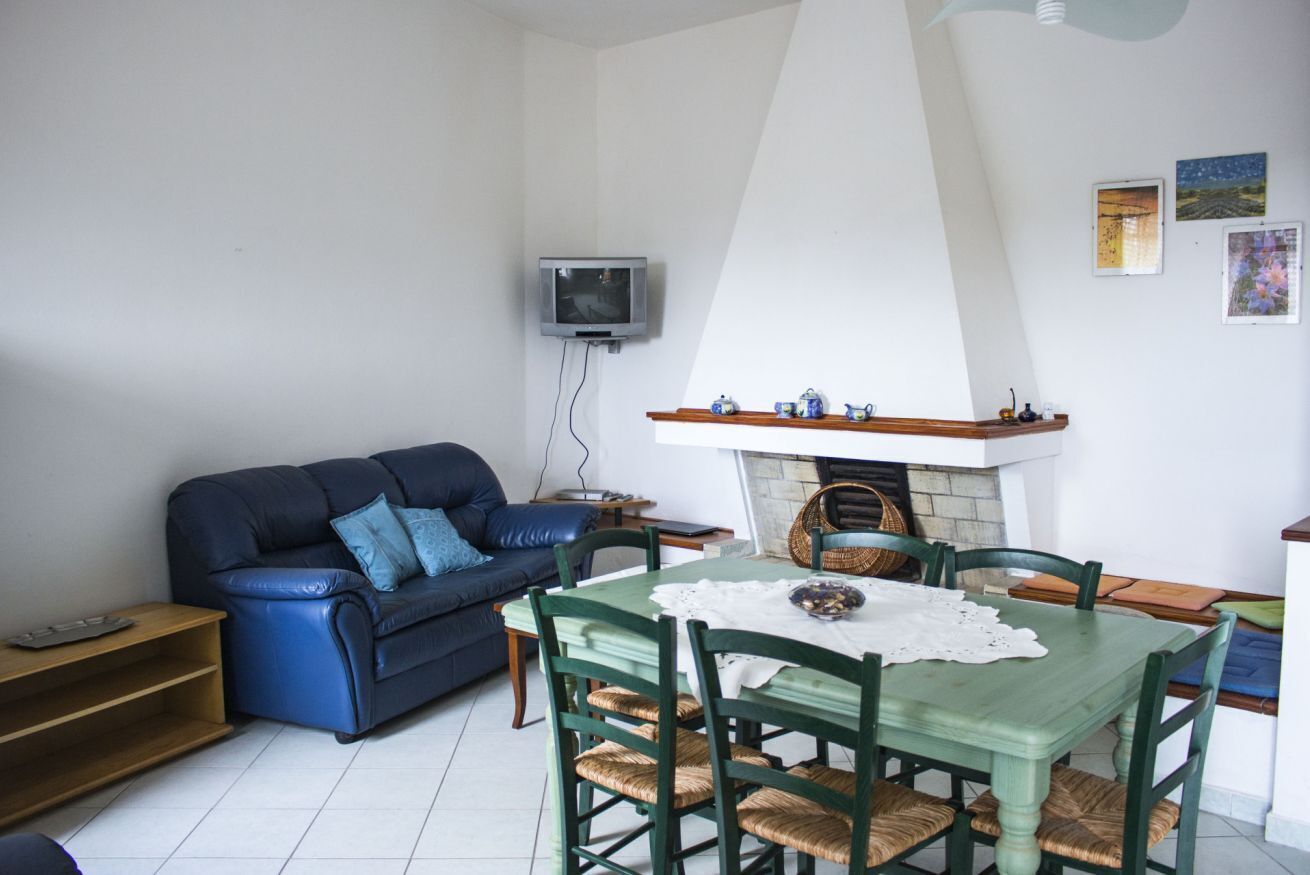 Una sala de estar con un sofá azul, una mesa de comedor con sillas, una chimenea y un televisor montado en la pared.