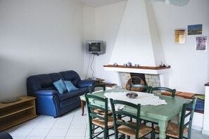 Un salon avec un canapé bleu, une table à manger avec des chaises, une cheminée et un téléviseur fixé au mur.