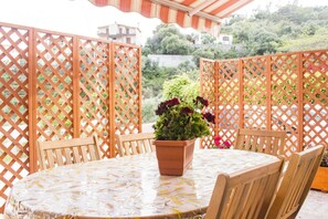 Une table ronde recouverte d’une nappe à motifs floraux, entourée de chaises en bois, avec une plante en pot placée au centre.