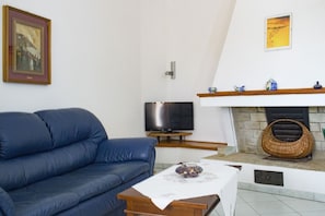Uma sala de estar com um sofá azul, uma TV de tela plana, uma lareira e um quadro pendurado na parede.