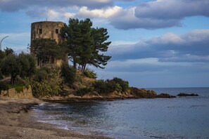 A coastal scene with a historical stone tower, rocky shoreline, and dense greenery.