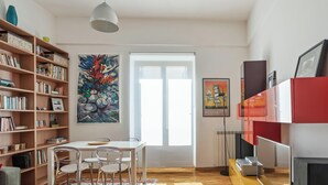 Een moderne woonkamer met een houten vloer, een eettafel met stoelen, een boekenkast, een groot schilderij, een rode en witte kast en een flatscreen televisie.