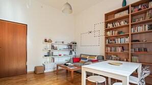 Een moderne woonkamer met houten vloer, een witte bank, een eettafel met stoelen en een boekenplank vol boeken.