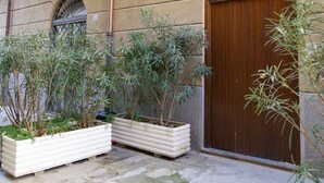 Een gebouw met een bruine houten deur, een balkon met metalen hekwerk en bloempotten ervoor.