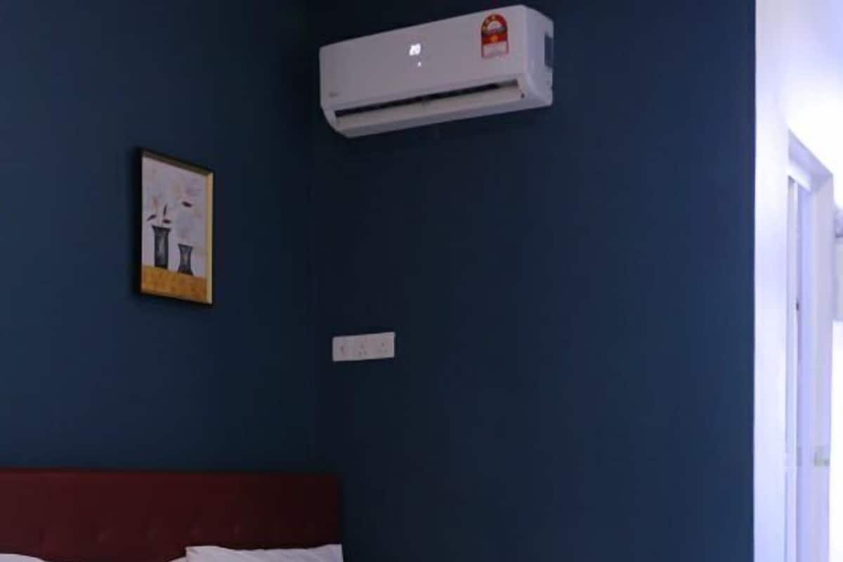 Quarto de hotel com duas camas, roupa de cama branca, cabeceira vermelha, unidade de ar condicionado e um quadro na parede.