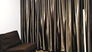 A room with a dark brown sofa, a wooden floor, and a large window with dark curtains. - The b'Hotel Kajang (Kajang)