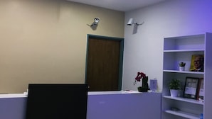 A reception area with a white reception desk, a wooden door, a shelf with plants and a framed picture, and a ceiling with blue LED lighting. - The b'Hotel Kajang (Kajang)