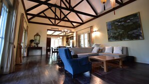 Amplia sala de estar con techo alto, vigas de madera, un sofá grande, un sillón azul y una pintura de nenúfares.