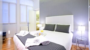 Une chambre d’hôtel avec un grand lit, deux tables de chevet avec des lampes, un radiateur et une fenêtre avec des stores.