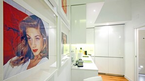 Une cuisine moderne avec des meubles blancs, un plan de travail et un évier. Un tableau encadré est accroché au mur, et une chaise blanche se trouve au premier plan.