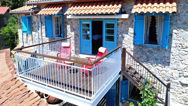 A stone building with a red-tiled roof, blue shutters, and a balcony with red chairs. - Kalopanayiotis Cottage  In The Centre (Nicosia)