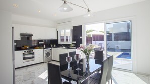 A modern kitchen with a dining area, large windows, and a view of the backyard. - Protaras Villa Hollywood Near To The Centre (Protaras)