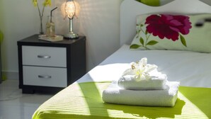 A neatly made bed with a floral pillow, a bedside lamp, and a stack of towels with a flower on top. - Protaras Villa Hollywood Near To The Centre (Protaras)