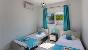 Un dormitorio con dos camas, una mesita de noche, una ventana con cortinas y una lámpara en el techo.