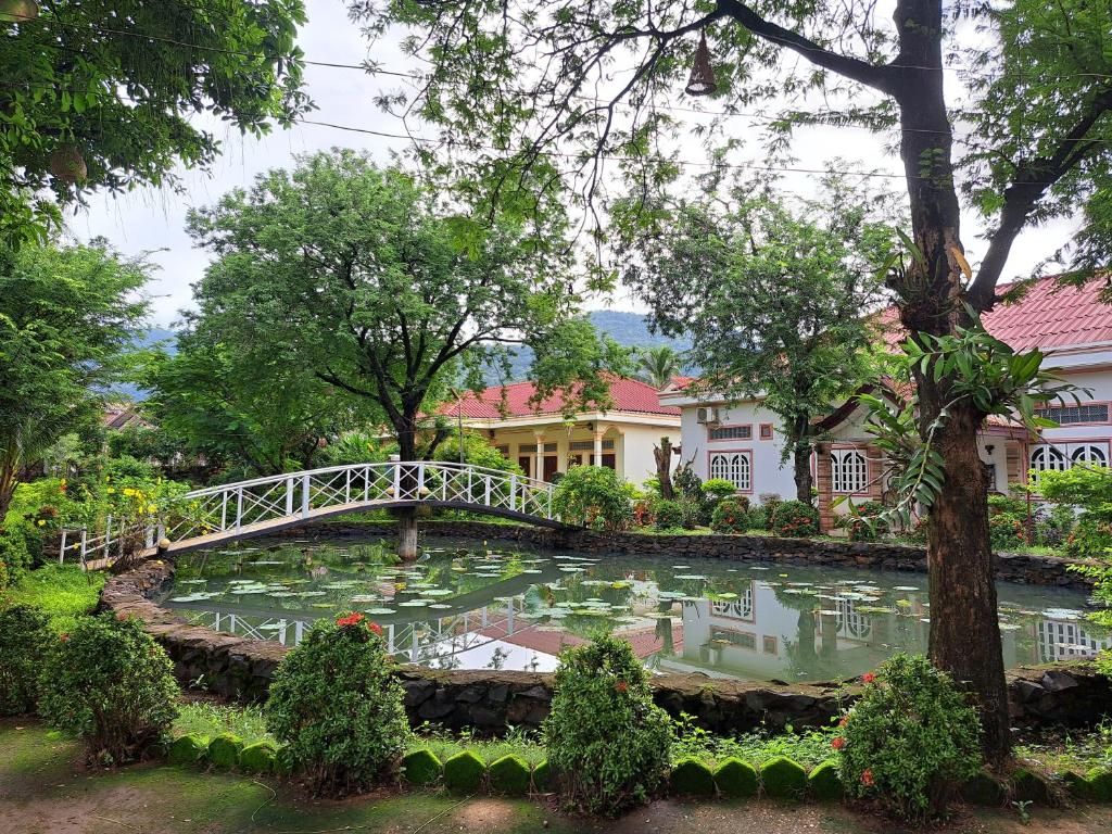 A pond with a bridge, surrounded by lush greenery and buildings with red roofs.