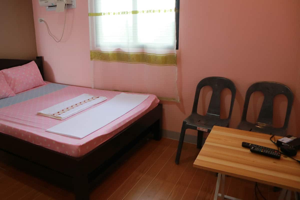 A bedroom with a bed, two chairs, a wooden table, and a window with blinds.
