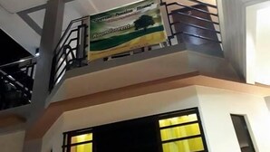 Ein mehrstöckiges Gebäude mit einem Balkon im oberen Geschoss, einem Schild, das ein Zimmer zur Miete anbietet, und großen Fenstern mit Vorhängen.