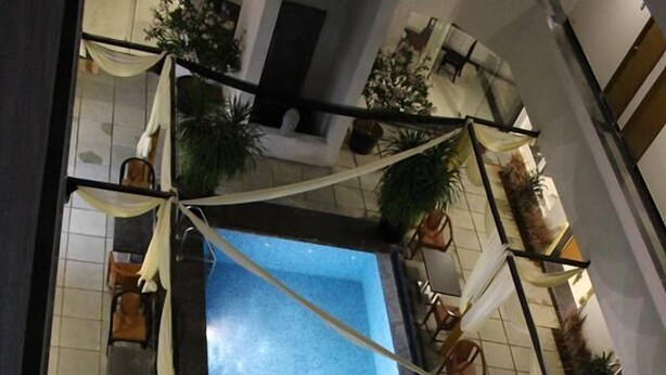 Un espace piscine aménagé sur le toit, avec des chaises et des tables, entouré de plantes en pot et agrémenté de tissus drapés.