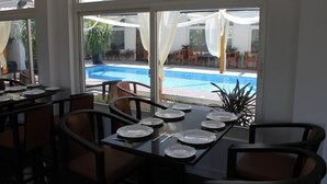 Un espace repas avec vue sur une piscine, de grandes fenêtres et des sièges à l’extérieur.