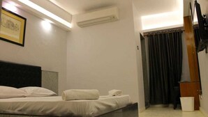 Une chambre d’hôtel avec un lit, un climatiseur fixé au mur, un tableau encadré et un rideau.