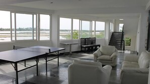 Une pièce spacieuse avec de grandes fenêtres, une table de ping-pong et un escalier menant à un autre niveau.