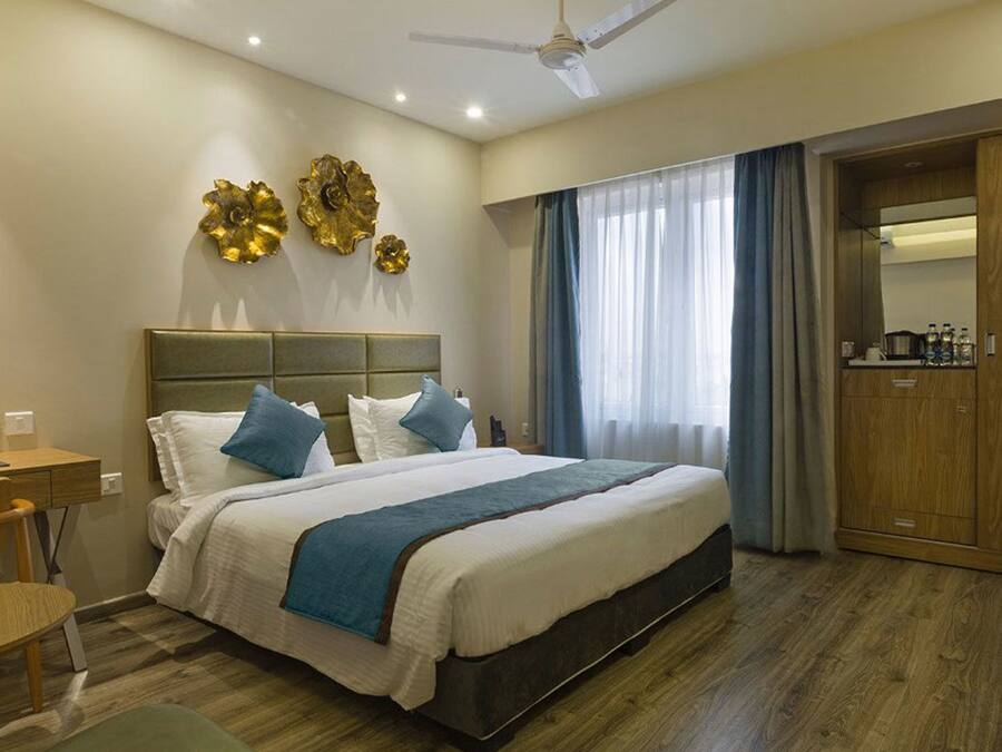 A hotel room with a large bed, a desk, a chair, a wardrobe, and a ceiling fan.