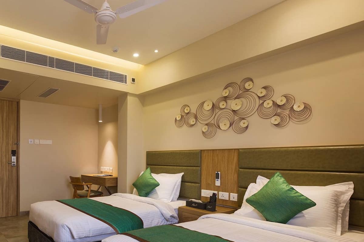 A hotel room with two beds, a desk, and a ceiling fan.
