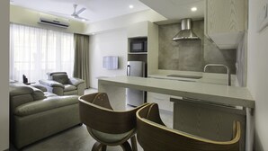 A modern hotel room with a kitchenette, a sofa, a wooden chair, and a flat-screen TV. - Floressa Randa (Chennai)