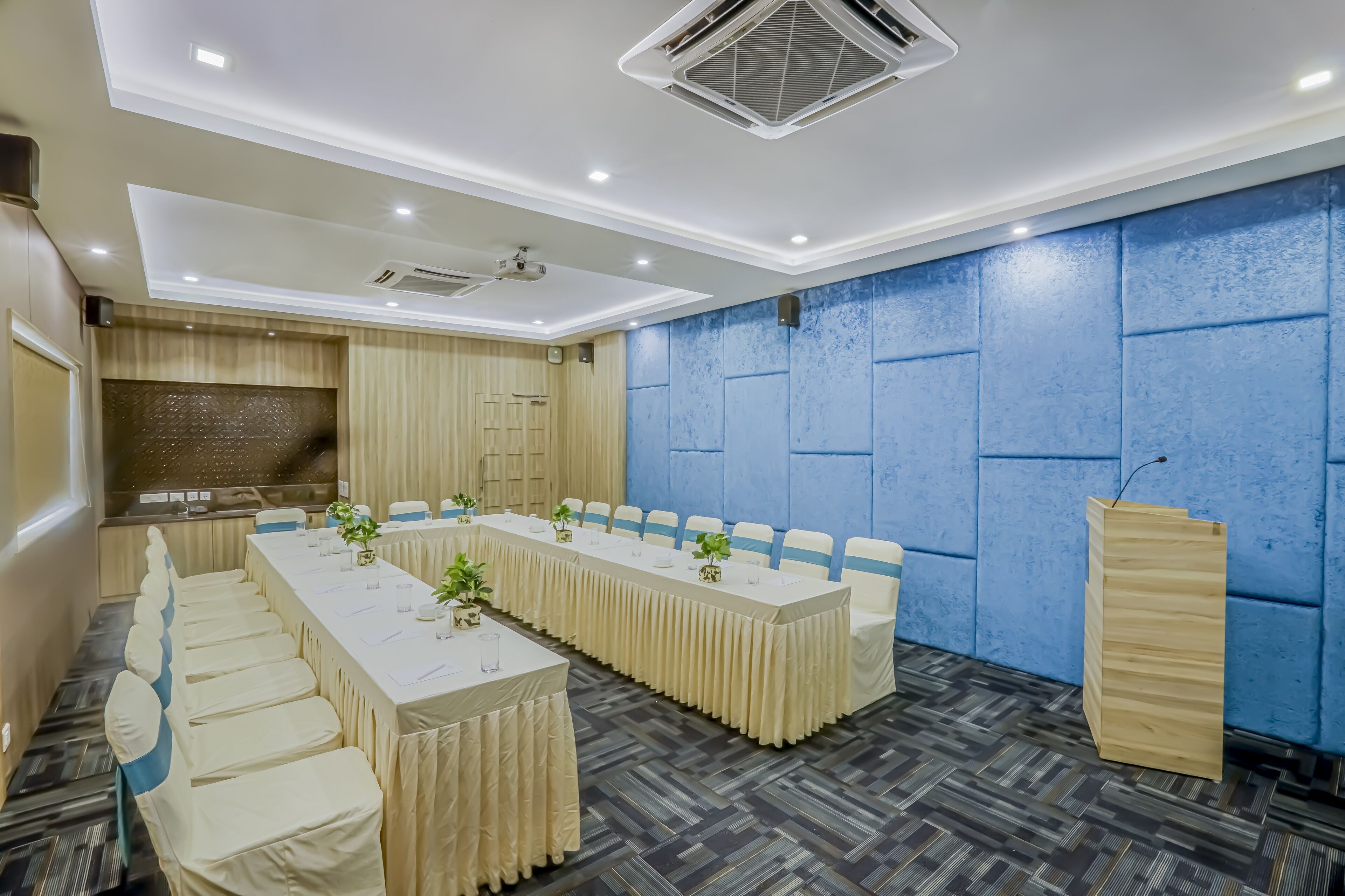 A conference room with a long table, chairs, a podium, and a blue textured wall.