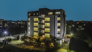 A multi-story building with balconies and illuminated windows, surrounded by trees and other buildings. - Floressa Randa (Chennai)