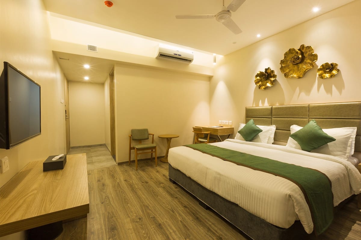 A hotel room with a bed, a desk, a chair, a television, and a wall-mounted air conditioner.