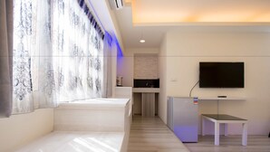 A modern hotel room with a bed, a TV mounted on the wall, a small table, and a kitchen area in the background. - FengJia Pandola (Taichung)