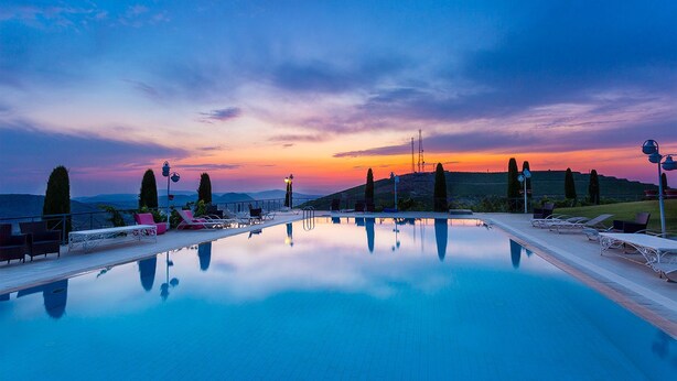 A serene outdoor swimming pool with lounge chairs and a sunset view. - Villa Estet Bag Oteli (Kula)